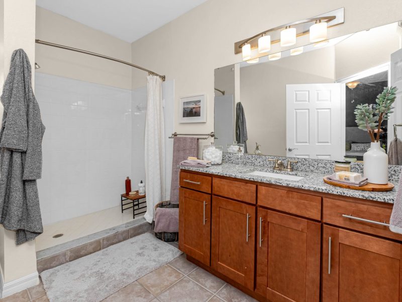Modern bathroom with wood vanity, granite countertop, and walk-in shower at TGM University Park.