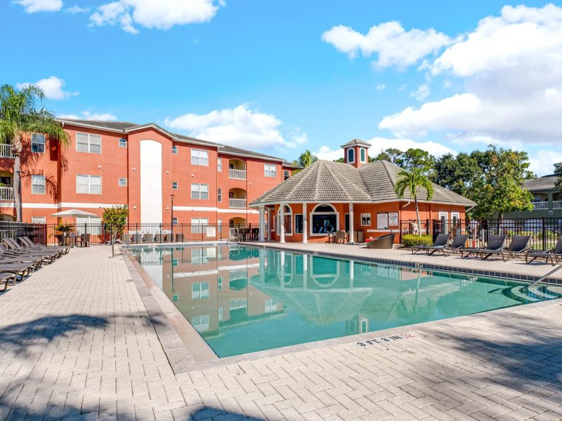 Resort-style pool with lounge chairs and clubhouse at TGM University Park apartments.