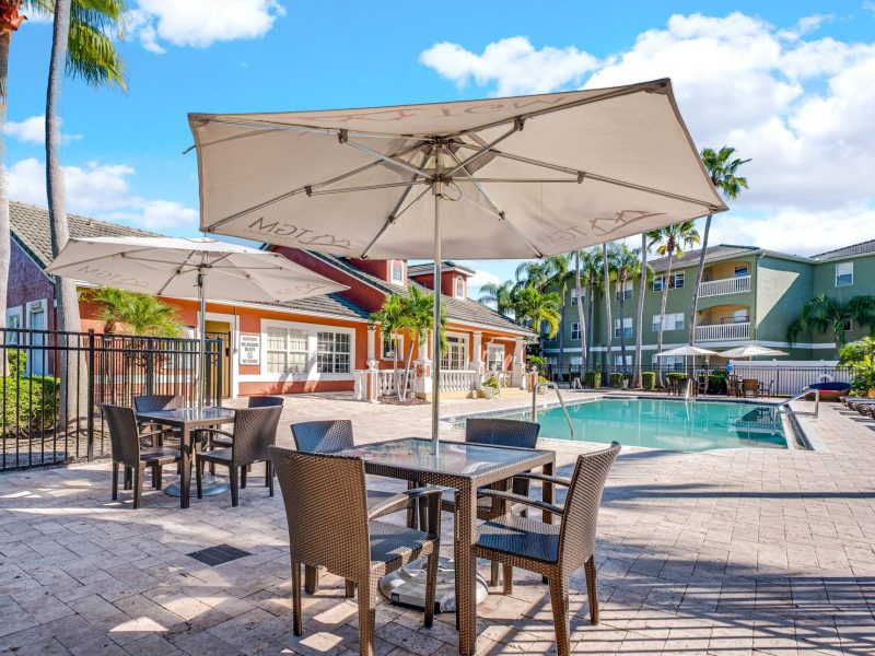 Outdoor pool and patio seating at TGM University Park with umbrellas and palm trees.