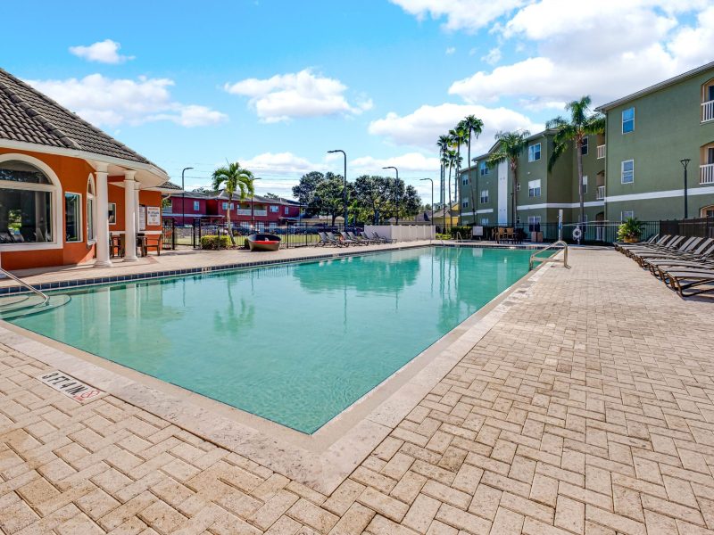 Luxury swimming pool and clubhouse at TGM University Park with palm trees and lounge chairs.