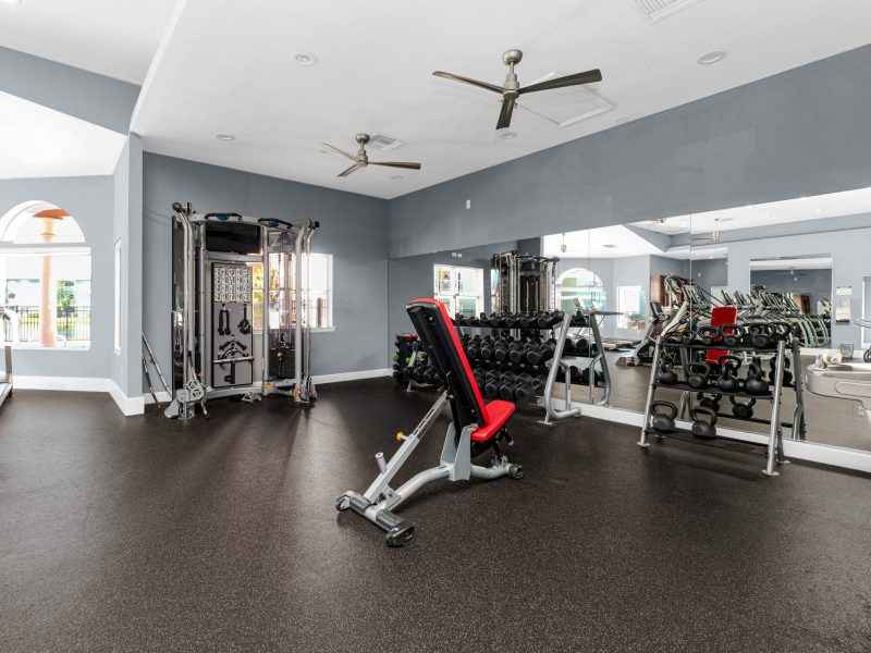 Modern gym at TGM University Park with weight bench, dumbbells, mirrors, and workout equipment.